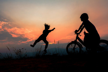 Silhouette of happy children playing jumping on mountain at sunset, summer time