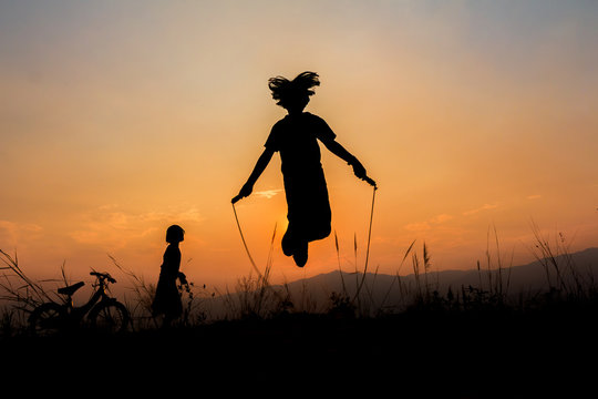 Silhouette Of Little Girl Jump Rope On Mountain At Sunset, Summer Time