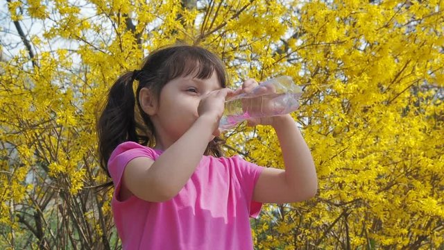 The child drinks water. A little girl is drinking water against a background of yellow flowers.