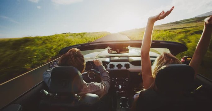 Couple driving into the sunset in convertible