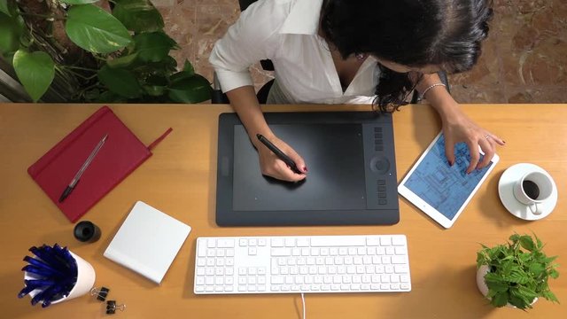 Female architect drawing building plan with graphic tablet talking on phone. Caucasian interior designer planning apartment layout at computer. Woman drawing restoration of house using digital devices