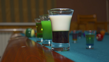 on a billiard table stand with coloured glasses of alcohol.