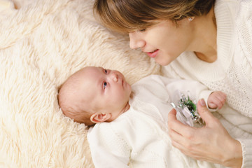 Mother and newborn daughter lie on pink plaid. They are dressed in warm knitted white sweaters. Mother and child look at each other