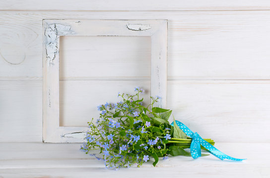 Forget-me-not flowers bouquet and vintage photo frame on white wooden shabby board