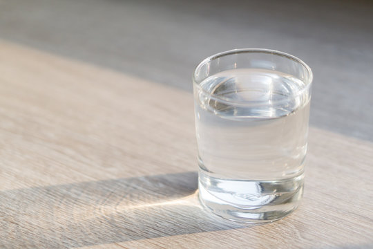 Glass of water on wood table with light in the morning, healthy care concept, selective focus