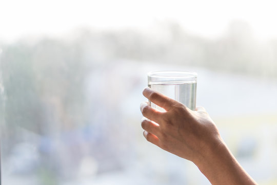 Hand holding glass of water with blur light in the morning background, healthy concept