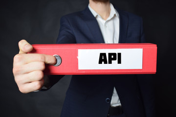 A businessman holds a folder with the inscription:API