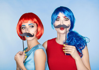  Females in red and blue wigs on blue background. Girls with false moustashes in hands