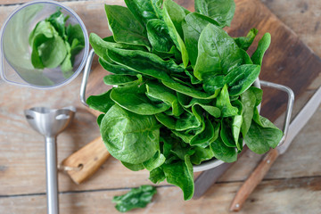 Fresh bunch of spinach leaves with blender for making sauce on wooden table close up, top view