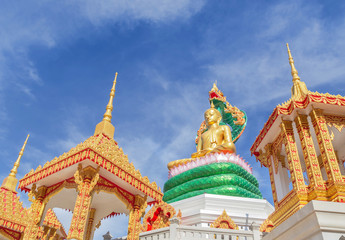 Fototapeta premium big golden buddha statue sitting under green thai dragon statue in thai temple on blue sky