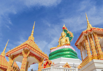big golden buddha statue sitting under green thai dragon statue in thai temple on blue sky