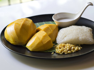 Southeast Asia and Thai traditional dessert, sweet mangos slices served with sweet and creamy sticky rice and coconut milk for summer fresh dessert in black plate