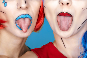 Females in red and blue wigs on blue background. Girls show each other tongues