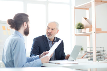 Mature businessman listening to his partner during a meeting. He is reading a report