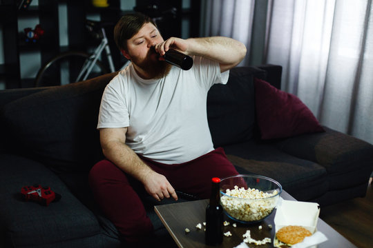Fat man drinks beer lying on the sofa