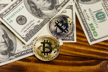 Golden and silver bitcoins and hundred dollar bills on wooden desk