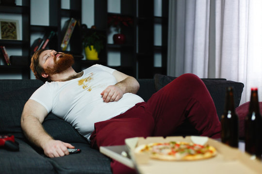 Ugly fat man sleeps on the couch after eating pizza and playing video-games