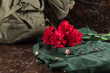 Military uniform and bag on a monument with red flowers