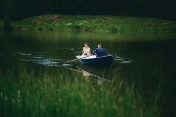 Fototapeta na wymiar beautiful young wedding couple, blonde bride with flower and her groom just married on small boat at pond
