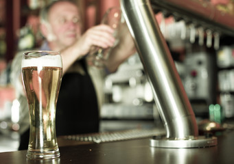 glass of beer on bar counter against background of friendly bartender