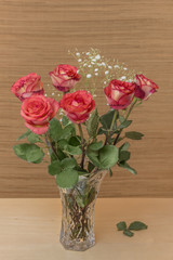 red roses with green leaves in a glass vase with water stand on a wooden table