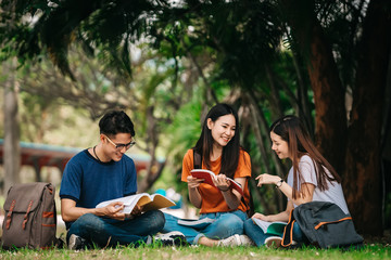 A group of young or teen Asian student in university smiling and reading the book and look at the tablet or laptop computer in summer holiday.