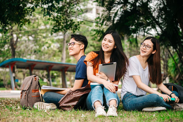 A group of young or teen Asian student in university smiling and reading the book and look at the tablet or laptop computer in summer holiday.