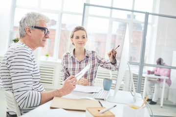 Businesswoman pointing at computer screen and discussing presentation with her coworker