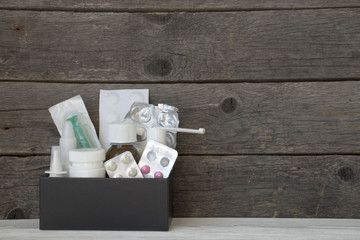 medicines in a black box on a wooden background, bandage, syringe, aerosol, pills, tablets