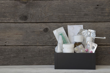 Fototapeta na wymiar medicines in a black box on a wooden background, bandage, syringe, aerosol, pills, tablets