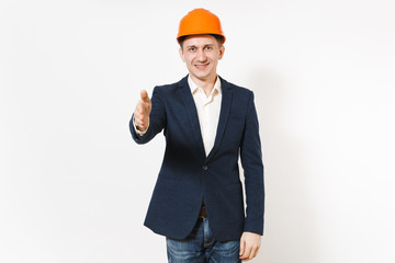 Young smiling businessman in dark suit, protective construction helmet standing with outstretched hand for greeting isolated on white background. Male worker, advertisement. Business, working concept.