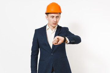 Shocked businessman in dark suit, protective construction orange helmet looking on clock on hand isolated on white background. Time is running out. Male worker for advertisement. Business concept.