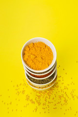Various spices in bowls on yellow background