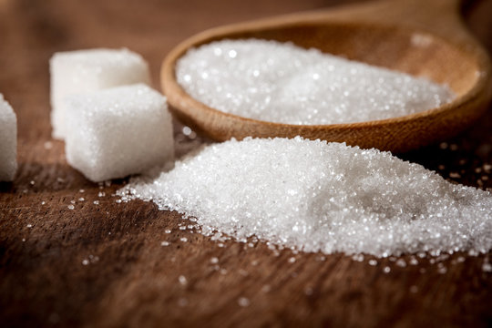 Close up a sugar cubes and cane in wooden spoon on the table