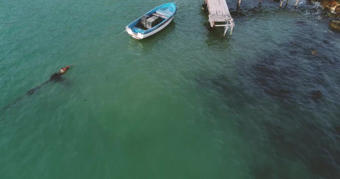 4k aerial video of lonely fishing boat and wooden pier in turquoise ocean, sea.