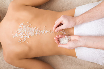 Beautiful woman lying and getting white sea salt scrub treatment in health spa. Masseur hands doing...
