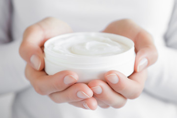 Obraz na płótnie Canvas Beautiful groomed woman's hands holding a white cream jar. Moisturizing cream for clean and soft skin. Healthcare concept.