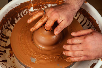 The hands of a man in clay on a potter's wheel mold a vase. potter works in a pottery workshop with clay