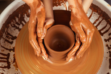 The hands of a man and a woman in clay on a potter's wheel mold a vase. The potter works in a pottery workshop with clay. the concept of Valentine's Day and love in pottery