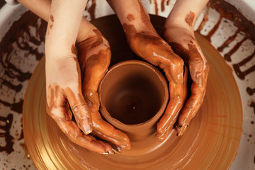 The hands of a man and a woman in clay on a potter's wheel mold a vase. The potter works in a pottery workshop with clay. the concept of Valentine's Day and love in pottery