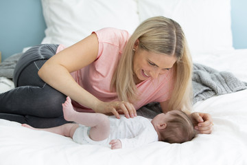 young, beautiful and blond mother with pink shirt is cuddling with her baby in bed