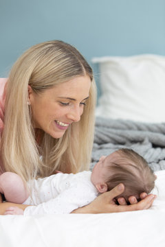 young, beautiful and blond mother with pink shirt is cuddling with her baby in bed