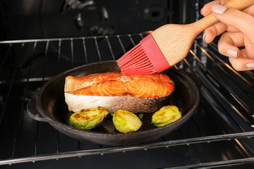Woman spreading sauce on fish fillet with brush in kitchen
