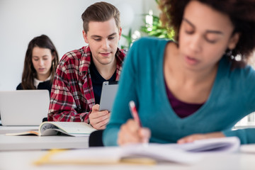 Young handsome student smiling with a nostalgic facial expression while using a tablet during class in a modern college or university