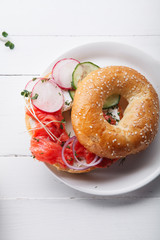 Bagels with salmon fish, cream cheese, cucumber and fresh radish slices on white wooden background