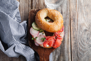 Bagels with salmon fish, cream cheese, cucumber and fresh radish slices on rustic gray wooden background
