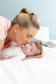 young, beautiful and blond mother with pink shirt is cuddling with her baby in bed