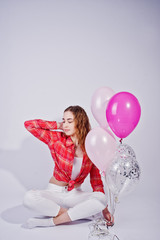 Young girl in red checked shirt and white pants with balloons against white background on studio.