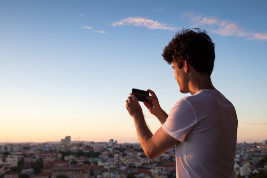 Man taking a photo of Lisbon skyline at dusk with mobile phone