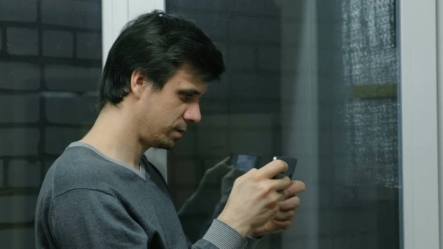 Man is playing games on a mobile phone on a balcony at night.